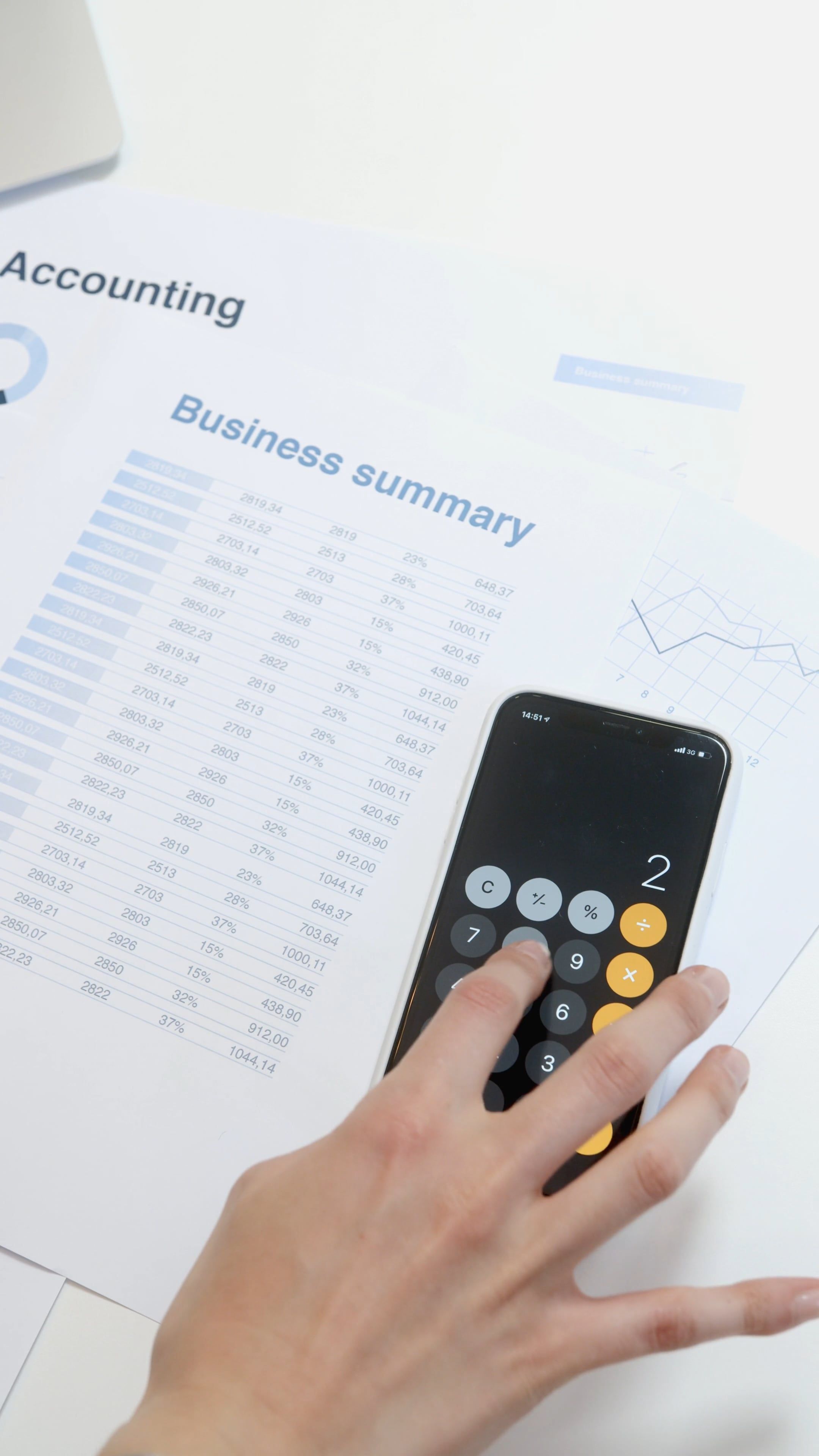 Une main utilisant une calculatrice noire sur fond de documents comptables avec toots imprimés et graphiques.